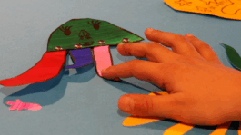 A Childs hand touching a creature made from coloured paper.